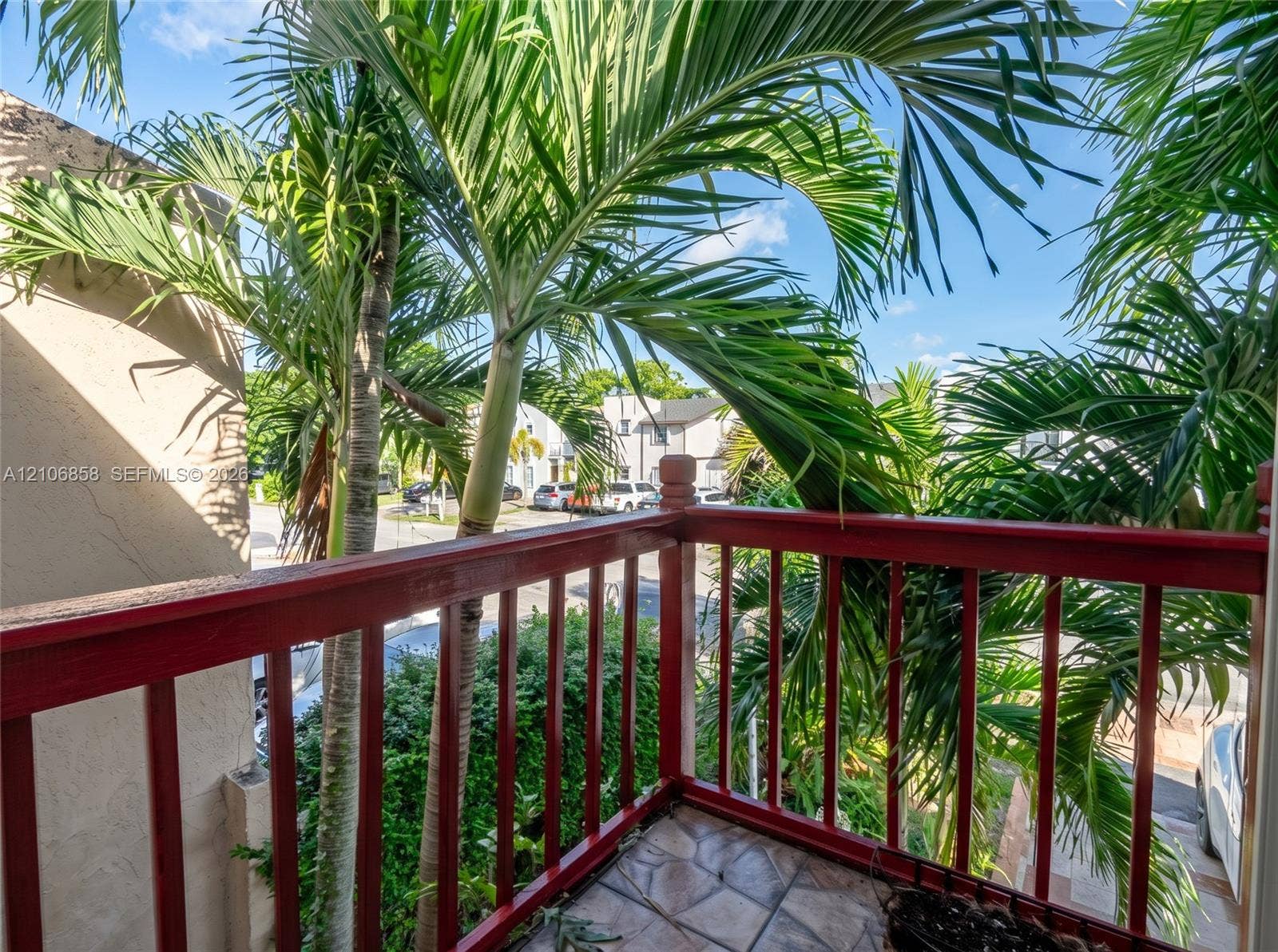 10960 SW 25th Street, Miami, FL 33165 Elevated balcony featuring a red-painted wood balustrade and tiled flooring, framed by mature palm trees