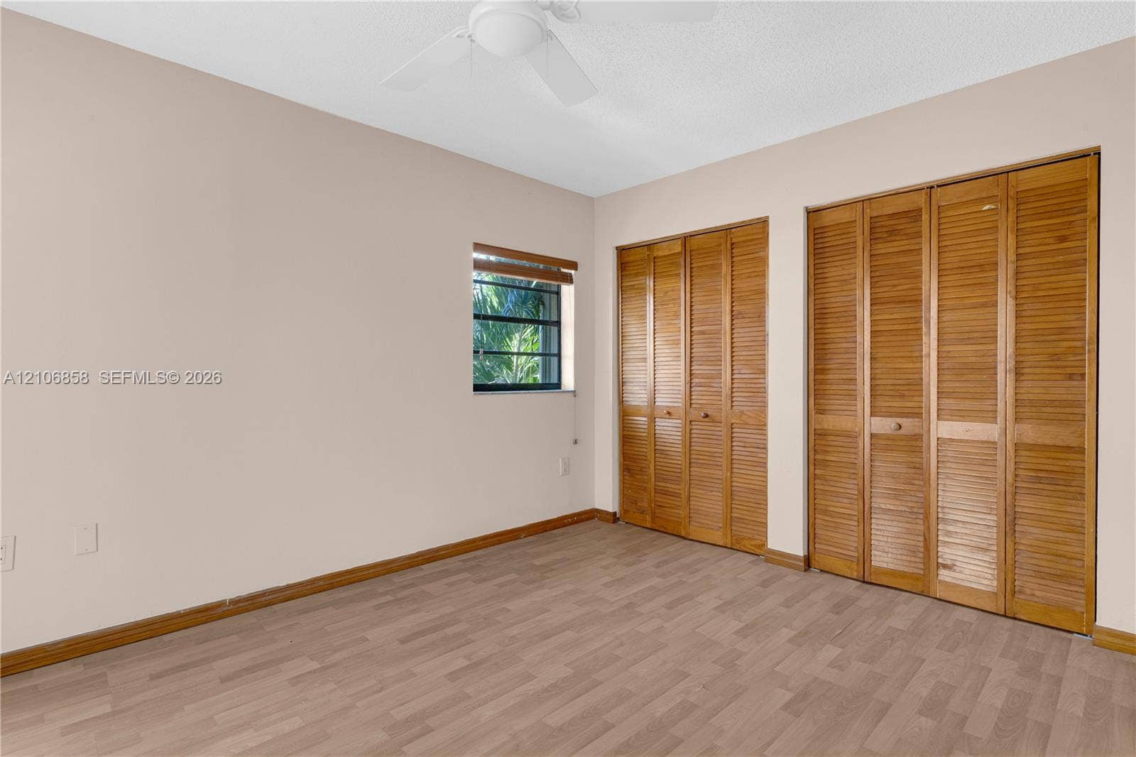 10960 SW 25th Street, Miami, FL 33165 Interior space featuring wood-finish flooring, two sets of bifold wooden closet doors, a ceiling fan with integrated lighting, and a window with wood-slat blinds