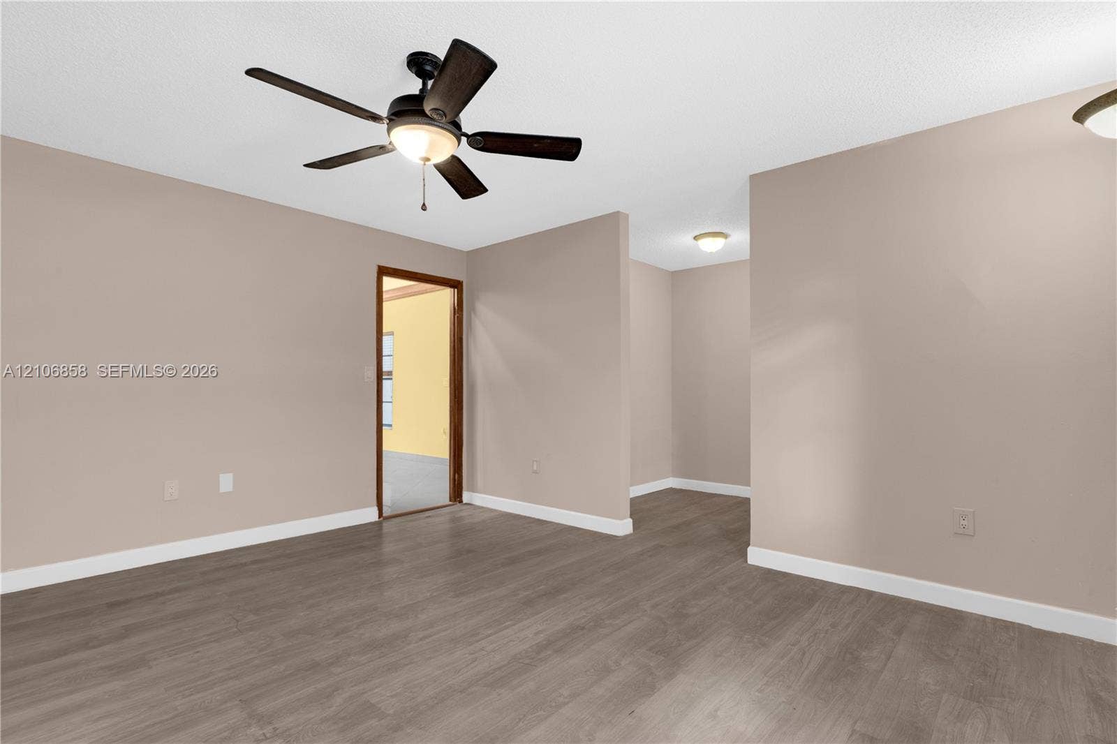 10960 SW 25th Street, Miami, FL 33165 Interior space featuring neutral-toned walls, wood-finish flooring, a five-blade ceiling fan with integrated lighting, and multiple flush-mount ceiling light fixtures