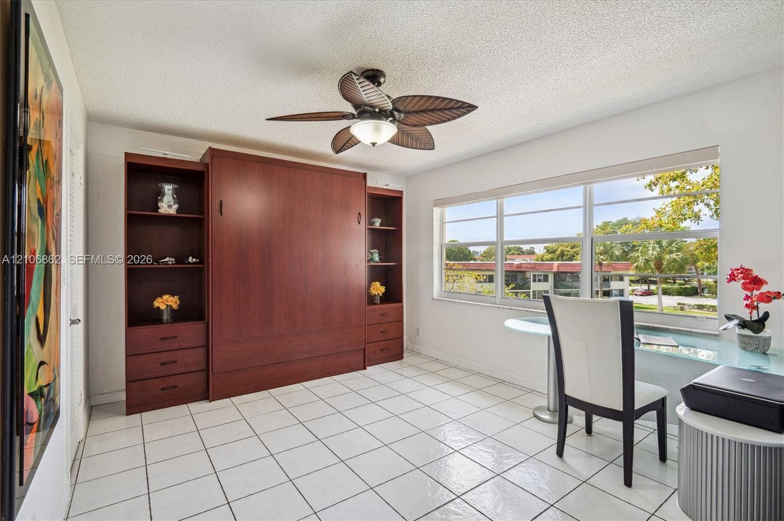 Built-in wood-finish cabinetry featuring open shelving and integrated drawer storage, ceramic tile flooring, and a ceiling fan with leaf-style blades