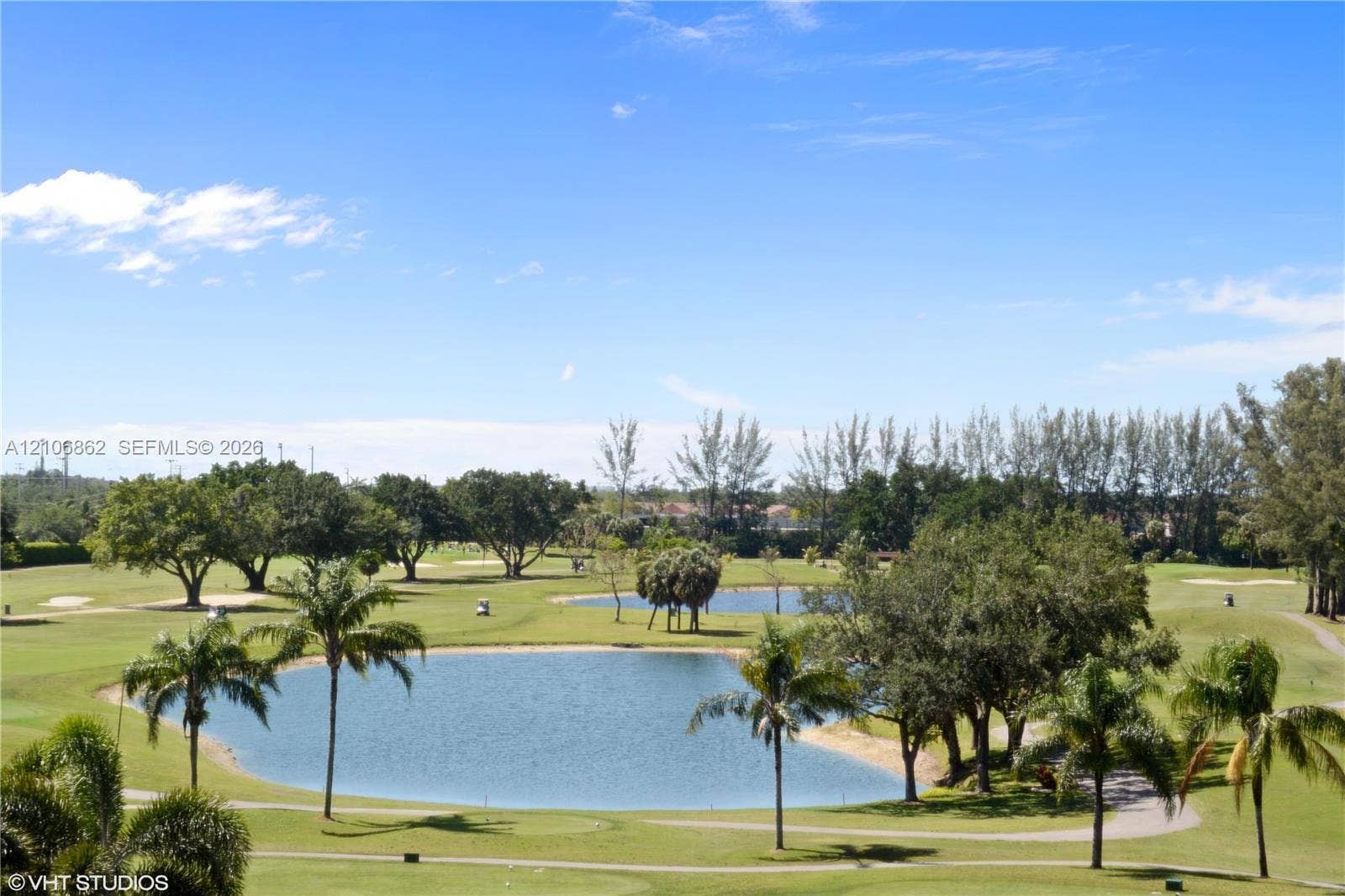 Expansive landscape featuring a golf course, multiple water features, manicured greens, and mature palm and hardwood trees