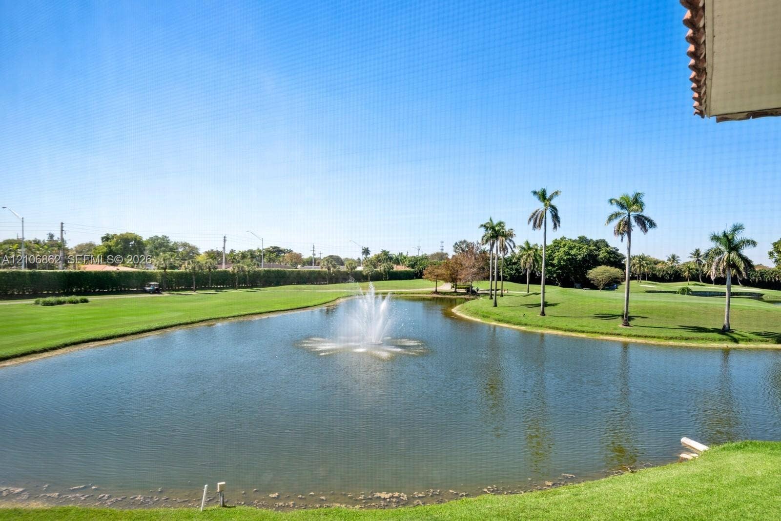 Screened-in outdoor area overlooking a water feature with a fountain, manicured lawn, and mature palm trees