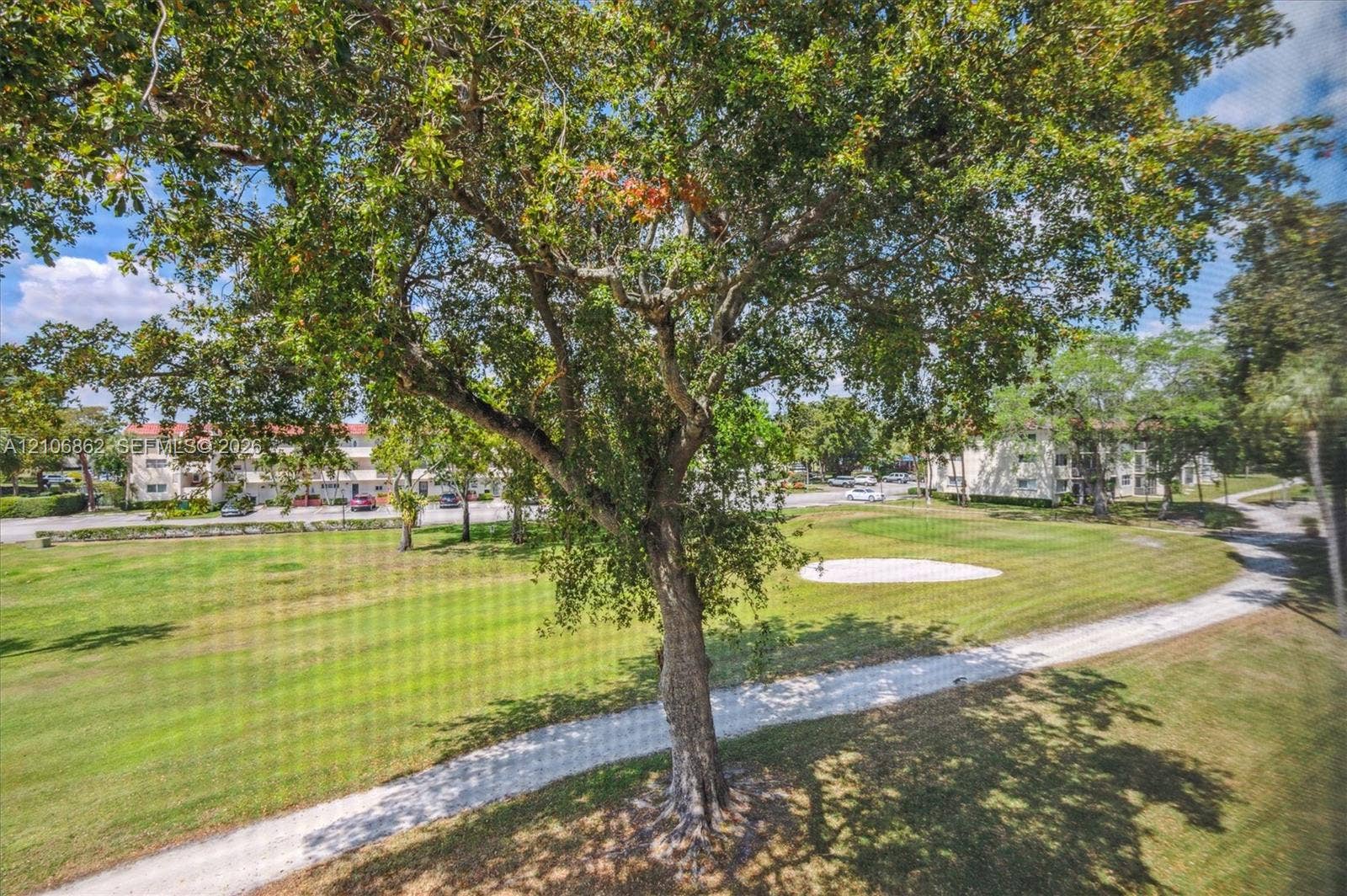 Expansive grounds featuring a manicured lawn, mature trees, a sand bunker, and a gravel pathway