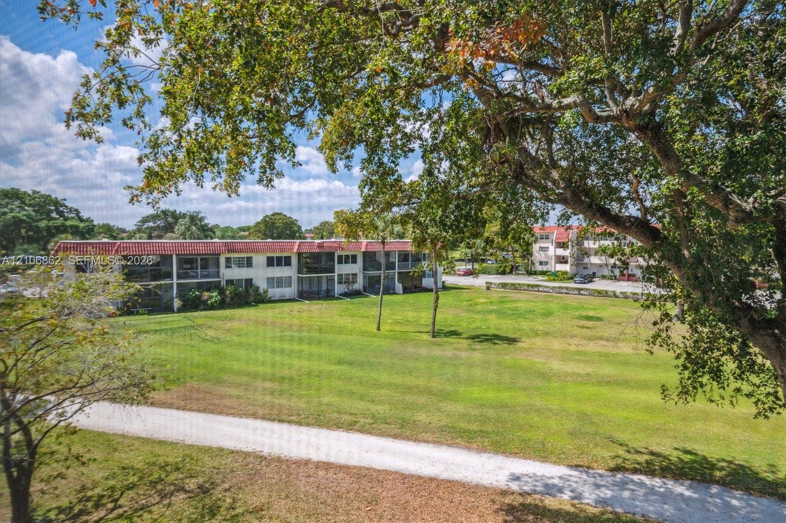 Expansive grassy common area featuring mature trees and a paved walking path