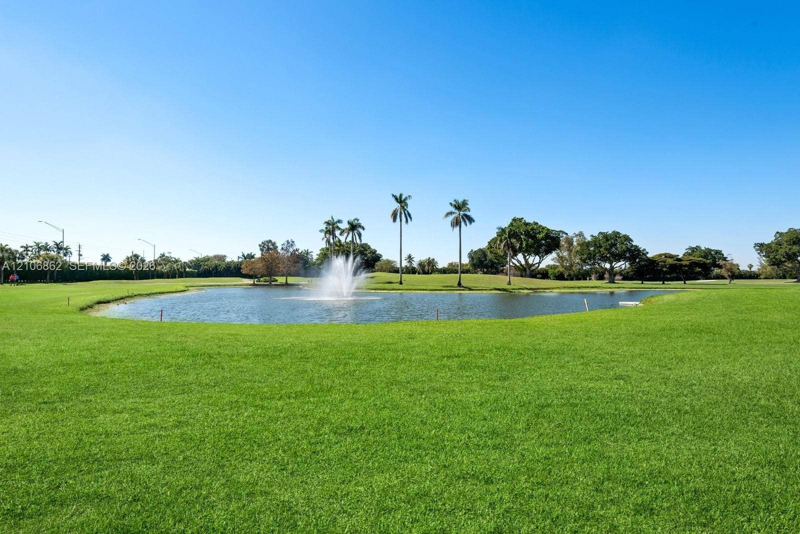 Expansive grounds featuring a manicured lawn, a central pond, a decorative water fountain, and mature palm trees