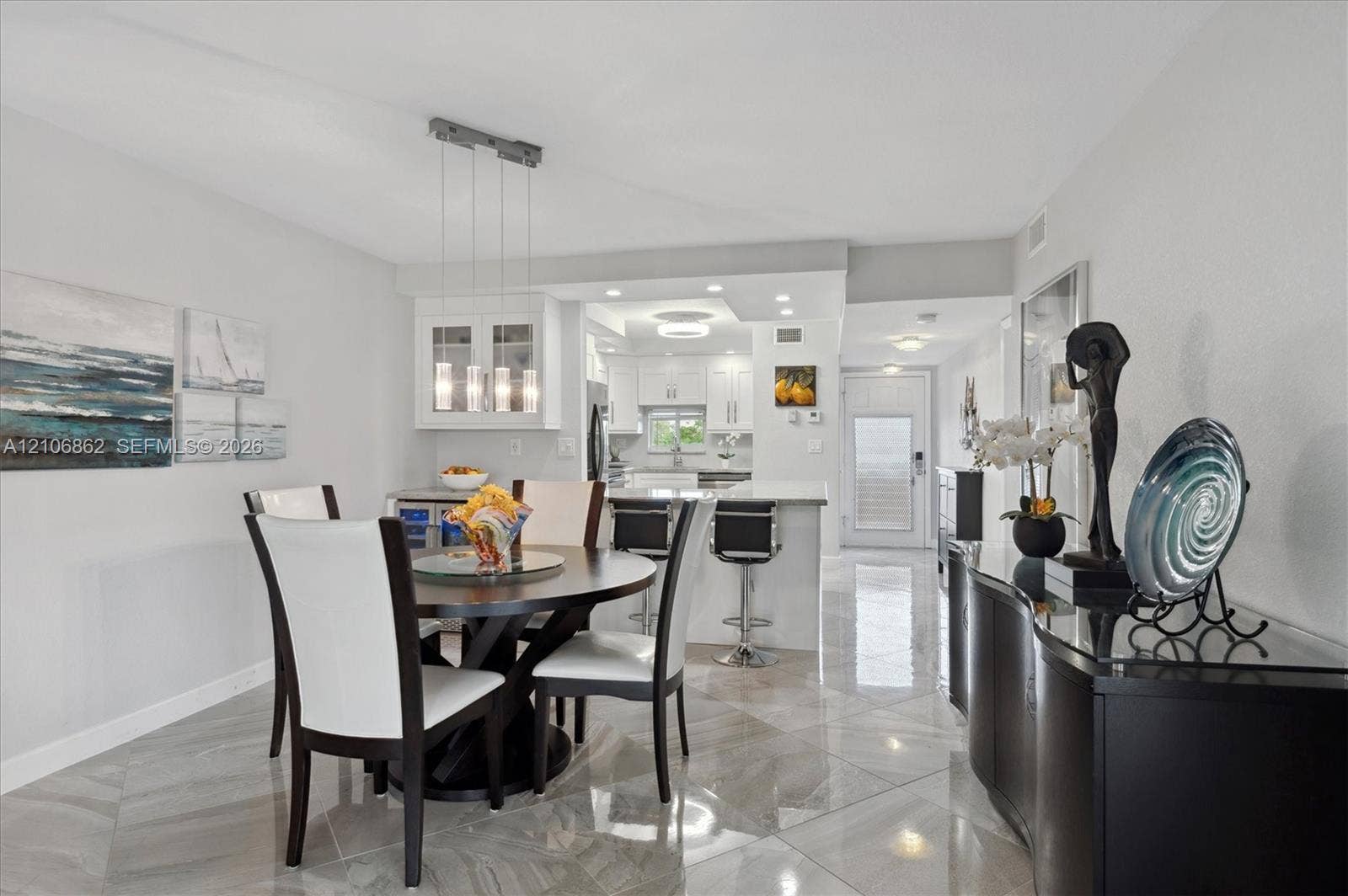Open-concept interior featuring large-format tile flooring, a multi-pendant light fixture, glass-front upper cabinetry, and a peninsula with bar seating