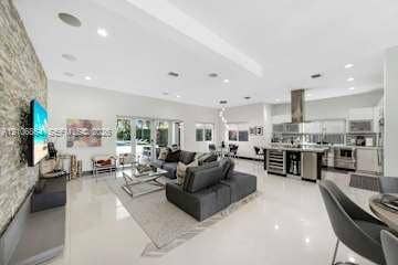 885 SW 144th Avenue, Miami, FL 33184 Open-concept living space featuring high ceilings with recessed lighting, large-format tile flooring, a floor-to-ceiling stone-veneer accent wall, and a kitchen equipped with a stainless steel range hood and built-in wine refrigeration
