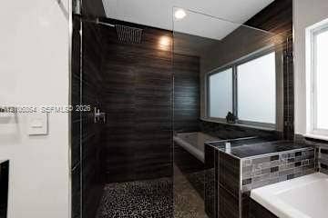 885 SW 144th Avenue, Miami, FL 33184 Walk-in shower with dark horizontal wall tile, pebble-texture floor, rain-style shower head, frameless glass enclosure, and a built-in soaking tub with mosaic tile surround