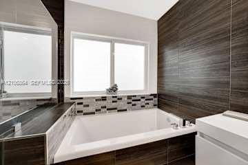 885 SW 144th Avenue, Miami, FL 33184 Built-in soaking tub with horizontal wood-finish tile surround, decorative stone-mosaic backsplash, and polished chrome faucet hardware