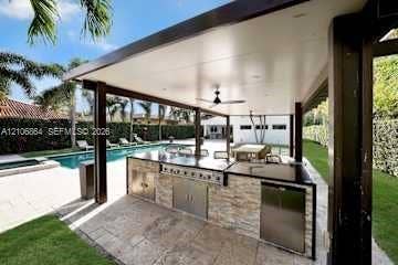 885 SW 144th Avenue, Miami, FL 33184 Covered outdoor kitchen featuring stone veneer cabinetry, stainless steel appliances, a flush-mount ceiling fan, and recessed lighting, situated by a swimming pool with stone paver decking