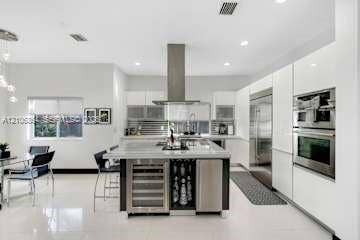 885 SW 144th Avenue, Miami, FL 33184 Kitchen featuring high-gloss white cabinetry, a center island with integrated wine refrigeration, stainless steel appliances including a built-in oven and microwave, and large-format tile flooring