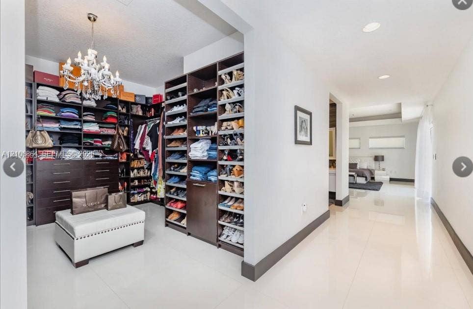 885 SW 144th Avenue, Miami, FL 33184 Custom dressing area featuring dark wood-finish built-in cabinetry, floor-to-ceiling shelving, drawers, and a ceiling-mounted crystal chandelier, complemented by polished tile flooring