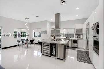 885 SW 144th Avenue, Miami, FL 33184 Contemporary kitchen featuring high-gloss cabinetry, a central island with integrated wine storage, a stainless steel chimney-style range hood, polished tile flooring, and built-in stainless steel double ovens