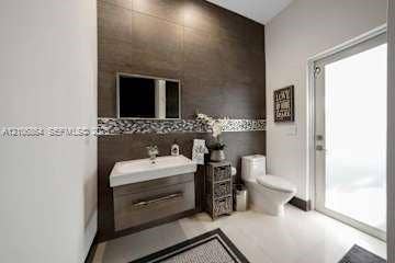 885 SW 144th Avenue, Miami, FL 33184 Wall-mounted floating vanity with integrated rectangular sink and wood-finish cabinetry, accented by floor-to-ceiling large-format wall tiling and a decorative glass mosaic tile border