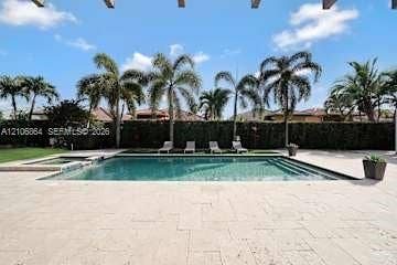 885 SW 144th Avenue, Miami, FL 33184 In-ground swimming pool with an integrated spa, surrounded by expansive stone paver hardscaping and mature palm trees