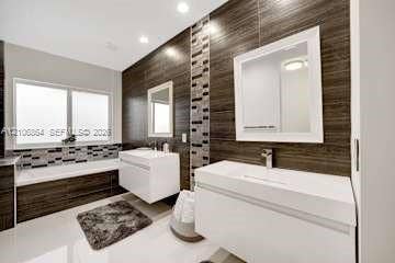 885 SW 144th Avenue, Miami, FL 33184 Dual floating vanities featuring white rectangular sinks and polished chrome faucets, complemented by horizontal wood-finish wall paneling, a glass mosaic tile accent strip, and a deep-soaking bathtub with a matching mosaic tile surround