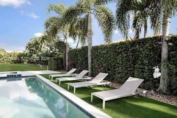 885 SW 144th Avenue, Miami, FL 33184 Rectangular swimming pool featuring a concrete deck and mature palm trees, bordered by a dense privacy hedge and synthetic turf area