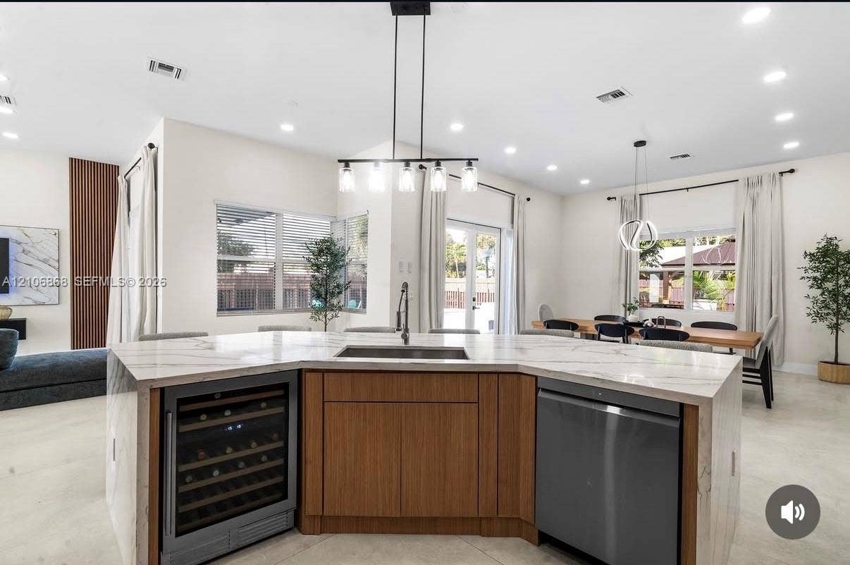 Kitchen island featuring a waterfall-edge countertop, undermount stainless steel sink, wood-finish cabinetry, built-in wine refrigerator, and stainless steel dishwasher