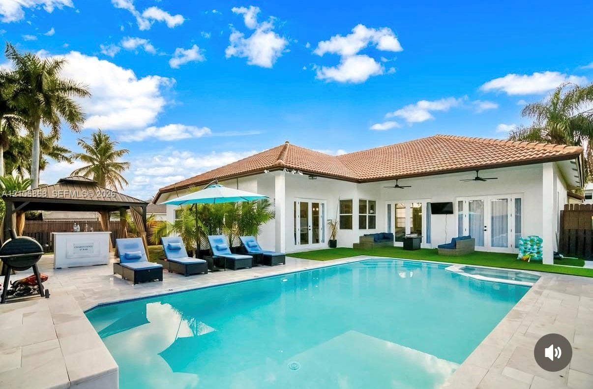 Outdoor area featuring an in-ground swimming pool with an integrated spa, stone-paver decking, and a permanent metal-roofed pavilion