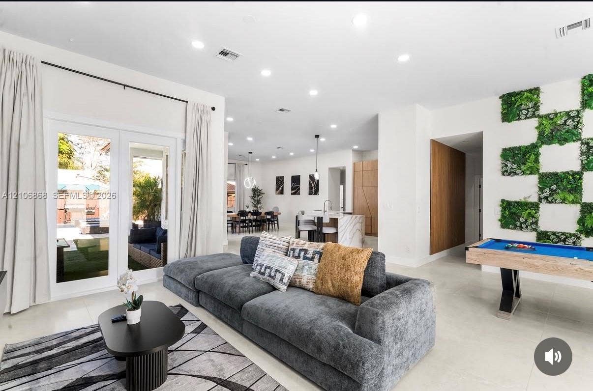 Open-concept interior featuring large-format tile flooring, recessed ceiling lighting, a decorative wall-mounted foliage feature, and double-glass paneled doors