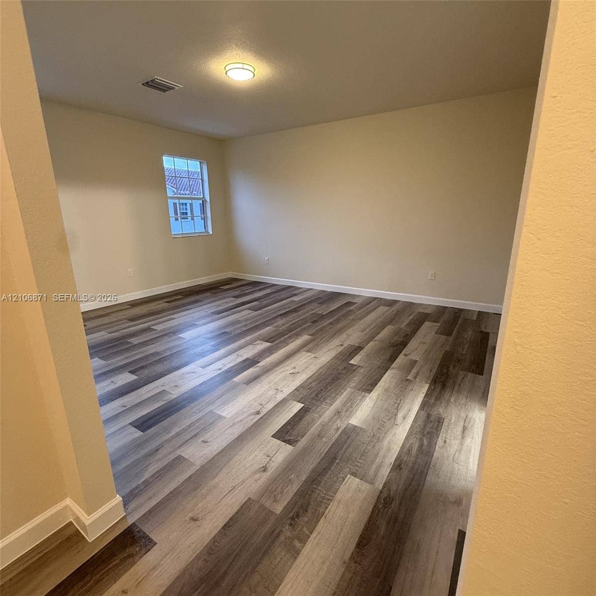 Interior room featuring wood-finish flooring, neutral wall paint, and a single-pane window with white trim