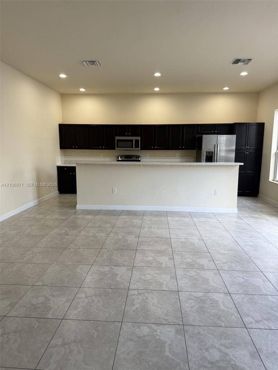 Kitchen featuring dark cabinetry, stone-finish countertops, stainless steel appliances, a breakfast bar, and tile flooring