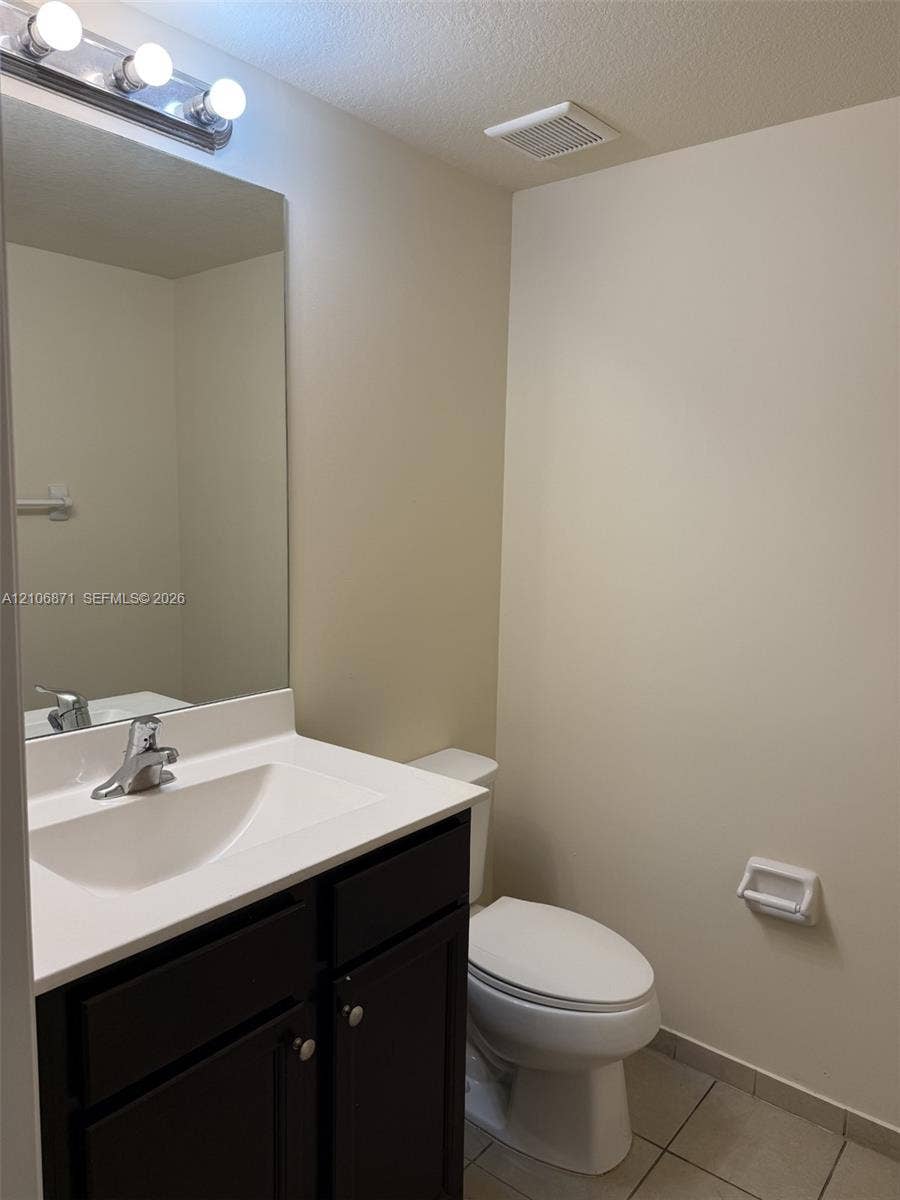 Dark-finish cabinetry with a white integrated sink and countertop, silver-toned single-handle faucet, large vanity mirror, and three-bulb vanity light fixture