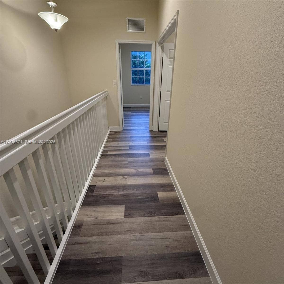 Hallway featuring wood-finish flooring, white spindle railings, and a pendant light fixture