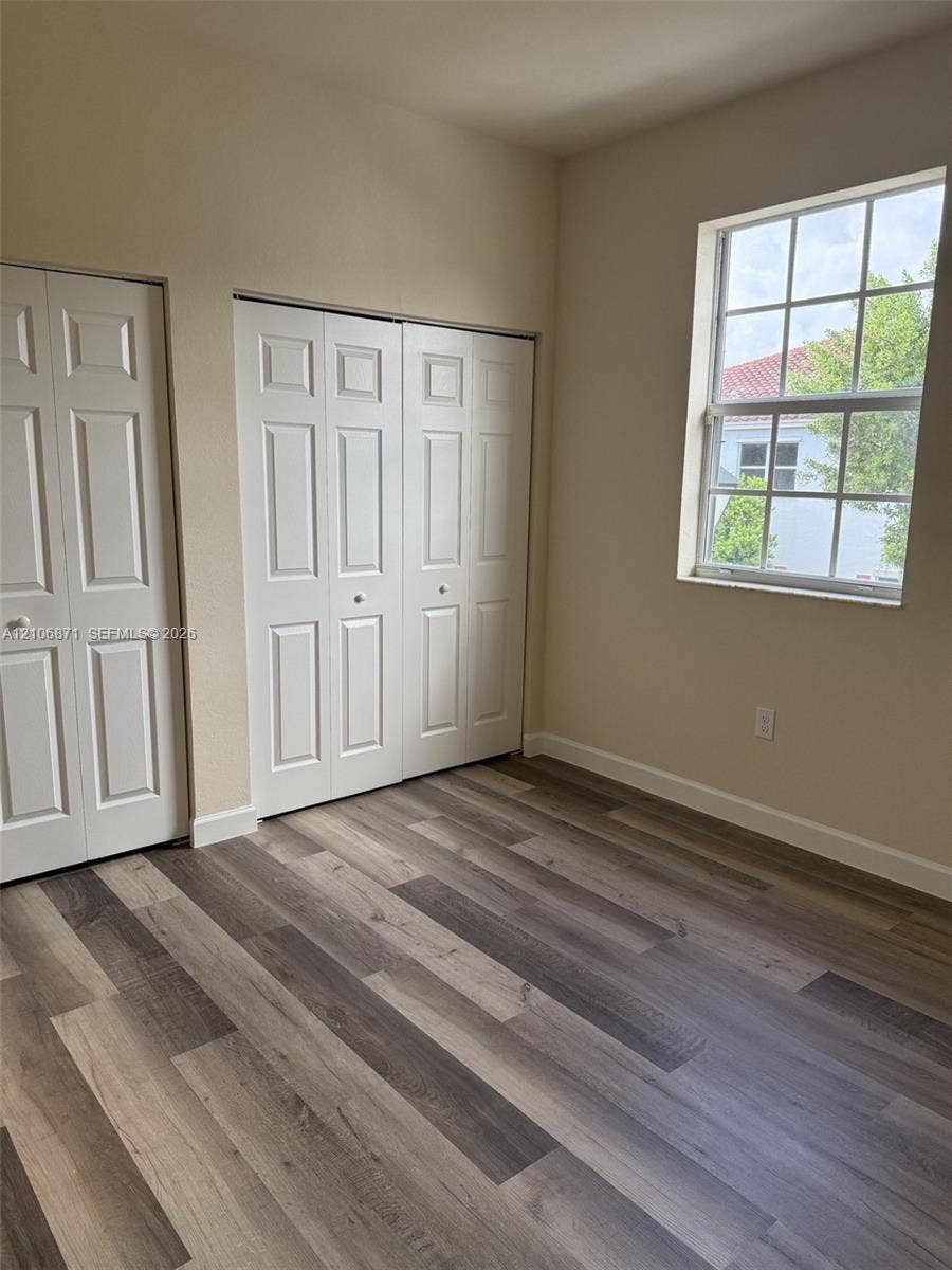 Interior room featuring wood-finish flooring, two sets of white paneled bi-fold closet doors, and a multi-pane window
