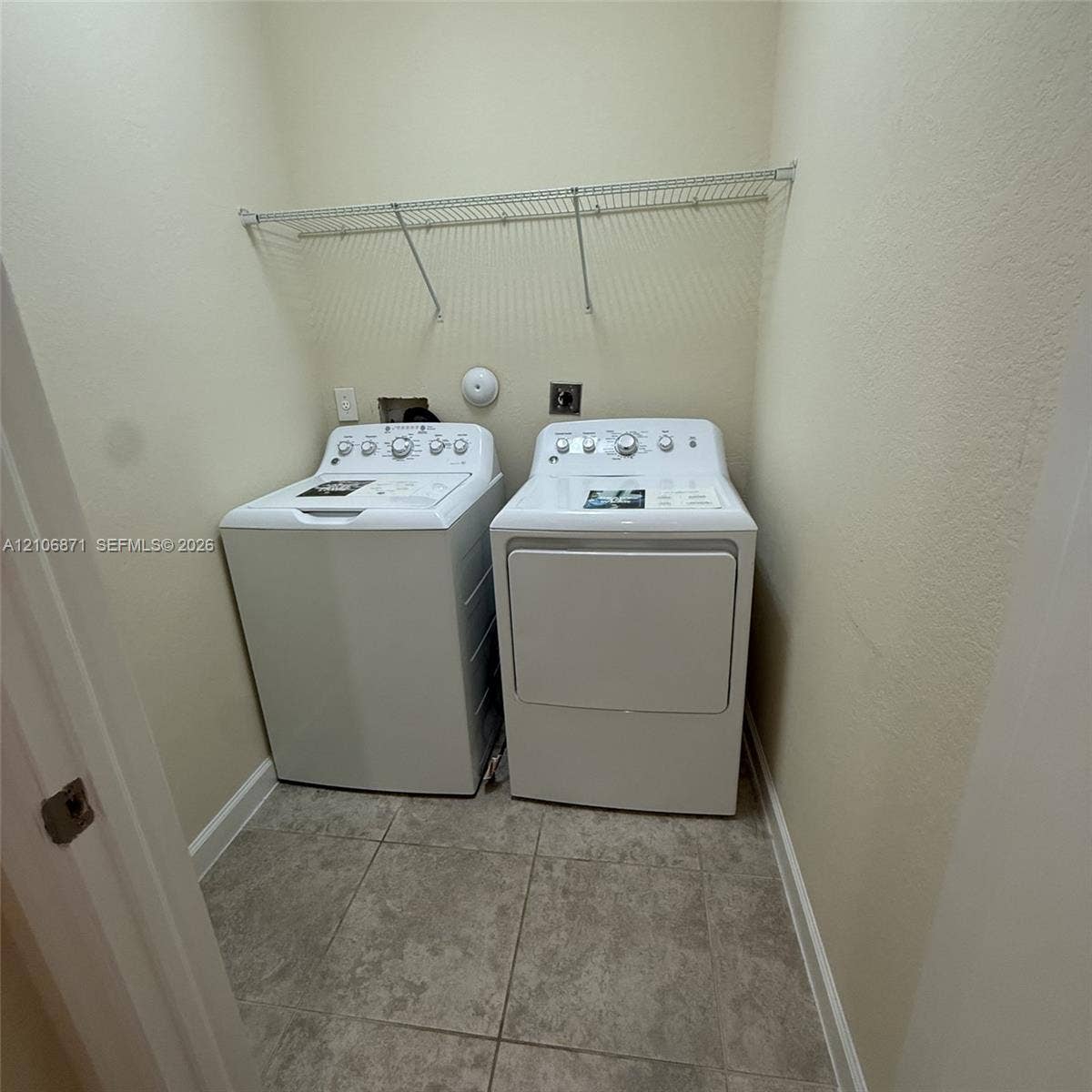 Laundry area featuring large-format ceramic tile flooring, neutral wall paint, and overhead wire shelving