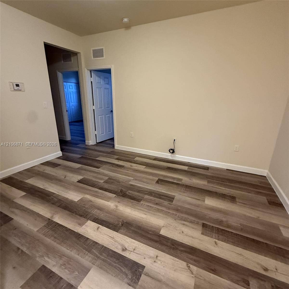 Interior room featuring multi-tonal wood-finish flooring, neutral wall paint, and white six-panel interior doors
