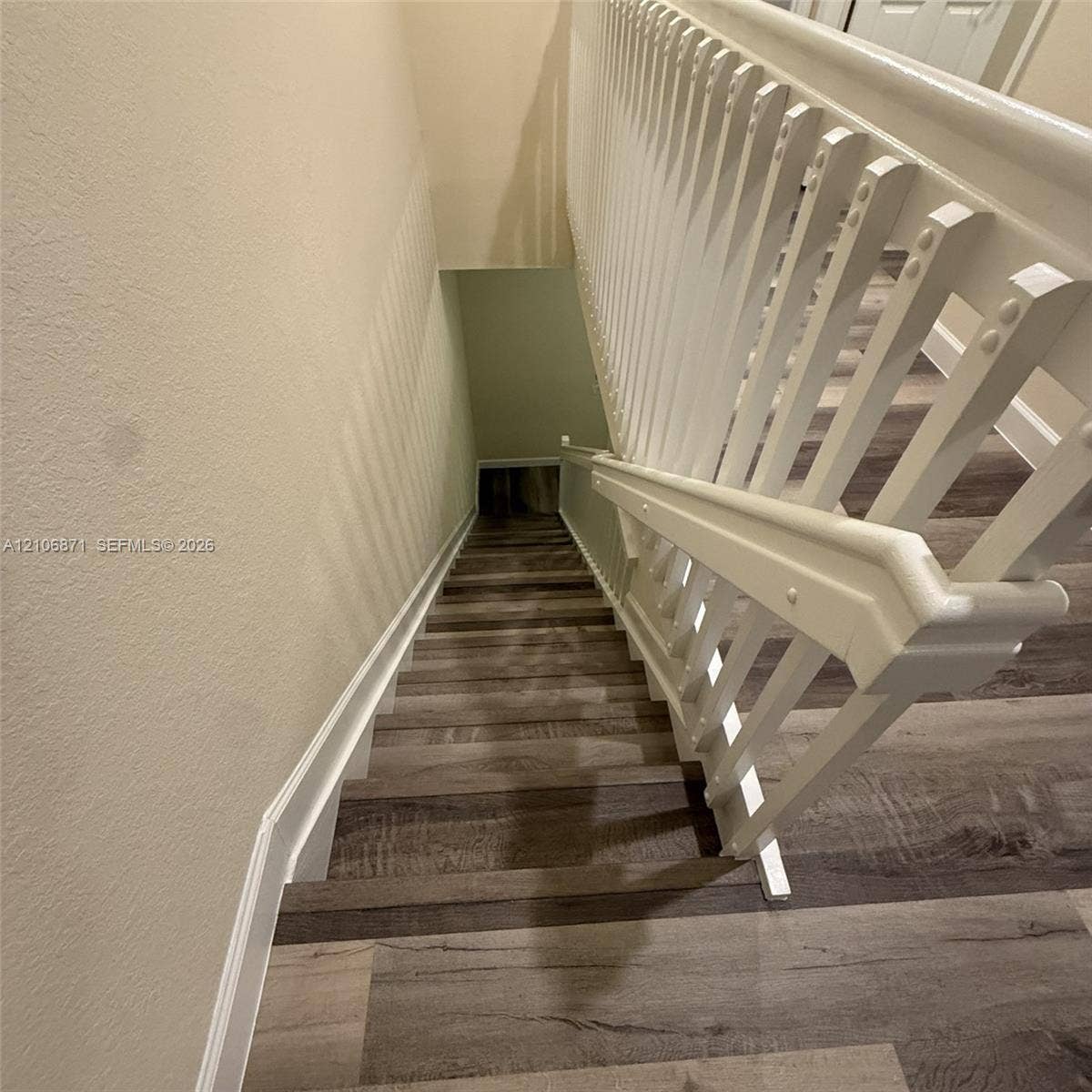 Staircase featuring wood-finish flooring, white wooden balusters, and a matching handrail