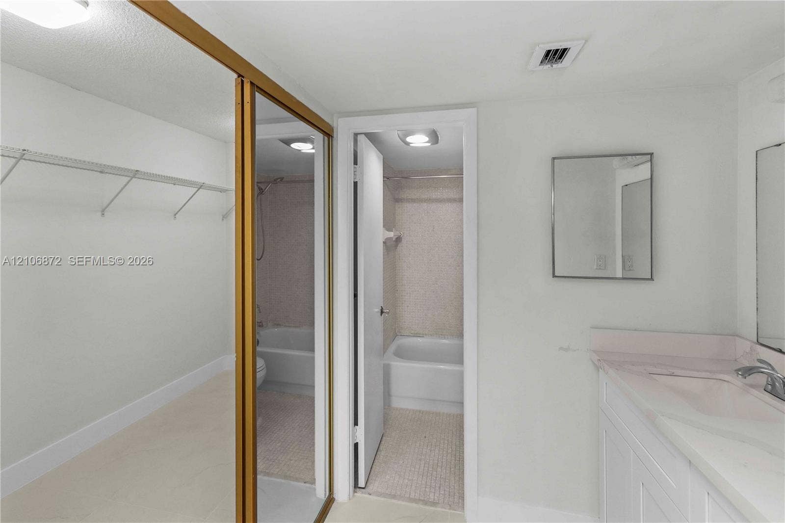 Full-length mirrored closet doors, solid-surface vanity countertop, undermount sink with chrome-finish faucet, recessed lighting, and tiled shower enclosure