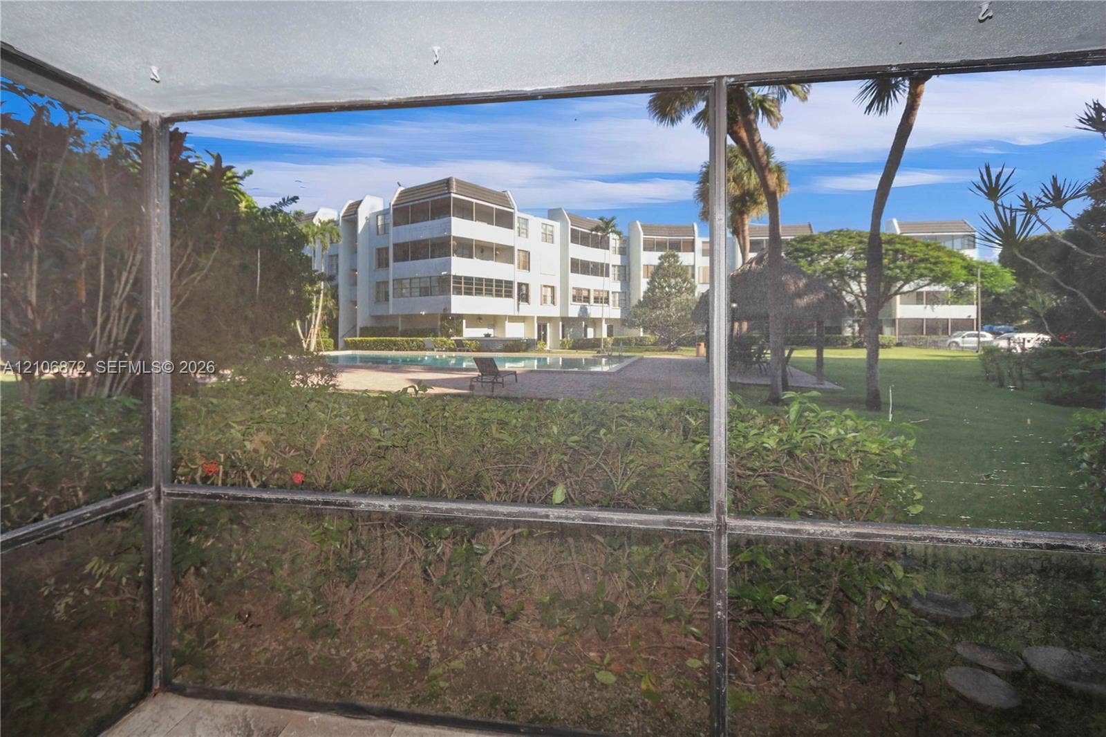 Screened-in patio with tiled flooring featuring a swimming pool, mature palm trees, and manicured landscaping