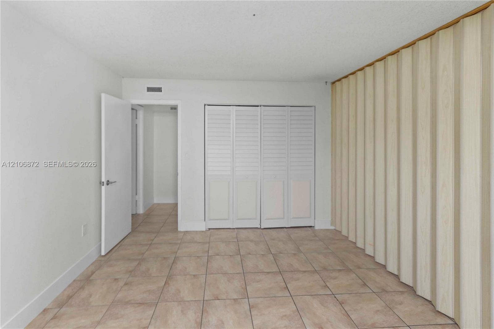 Room featuring ceramic tile flooring, built-in louvered-panel closet doors, and a wood-finish accordion partition wall