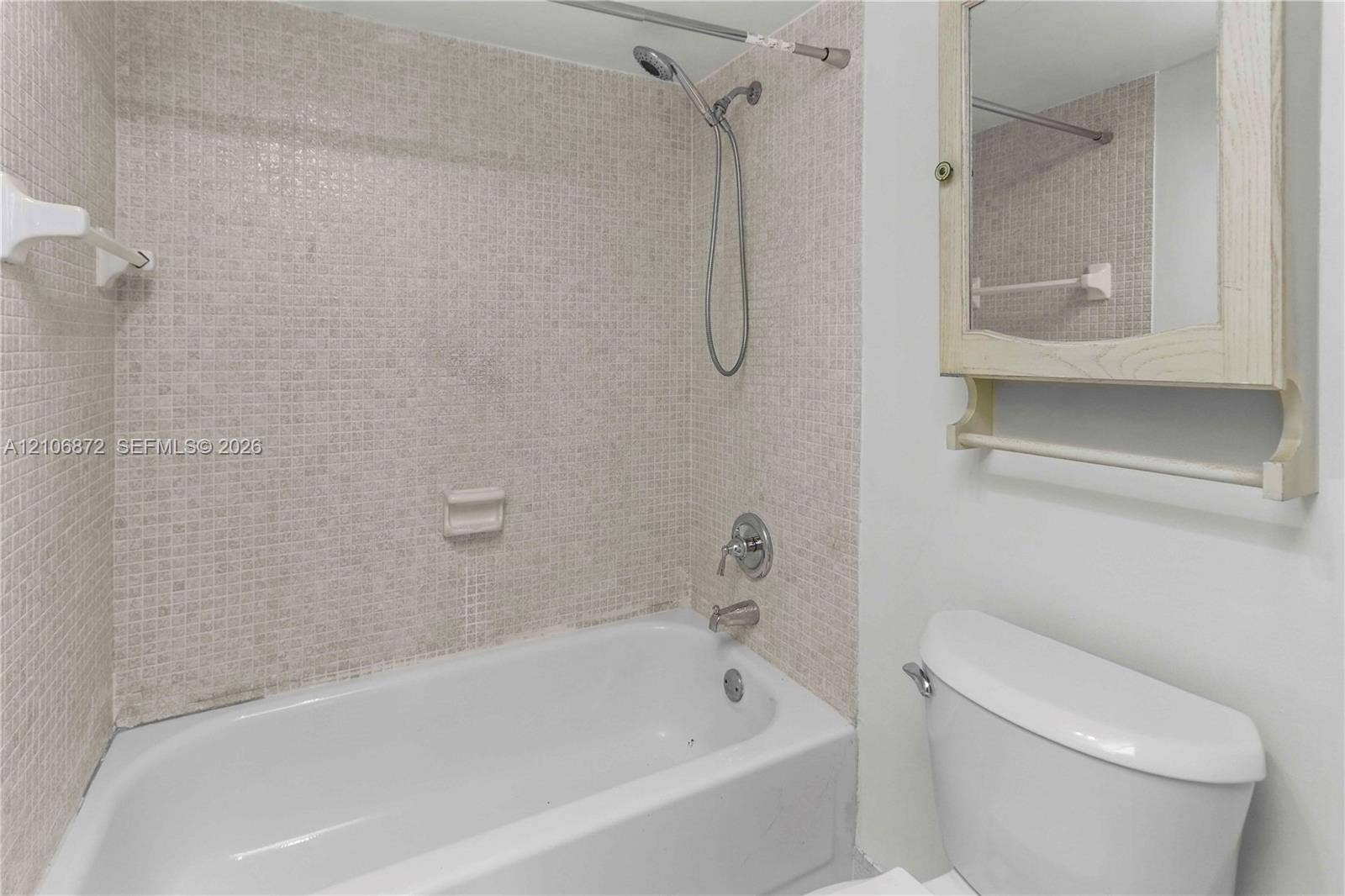 Bathtub with mosaic tile surround, adjustable handheld shower head, and wall-mounted medicine cabinet