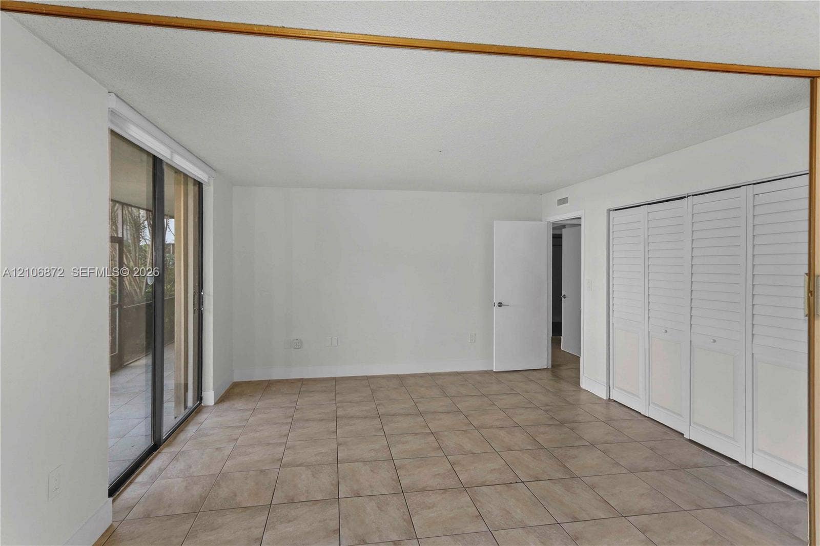 Neutral interior space featuring tile flooring, floor-to-ceiling glass sliding doors, and white louvered closet doors
