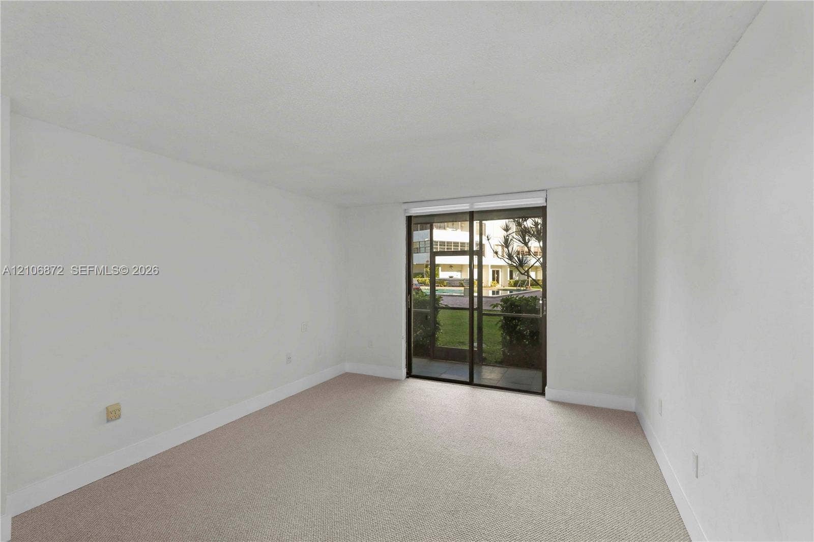 Neutral-toned interior space featuring light-colored wall-to-wall carpeting and floor-to-ceiling sliding glass doors with a screen panel