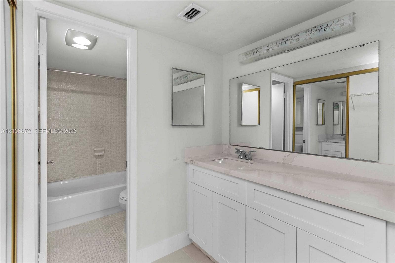 Bathroom featuring a vanity with white cabinetry and a stone-finish countertop, a large wall-mounted mirror, and a tile-surround bathtub