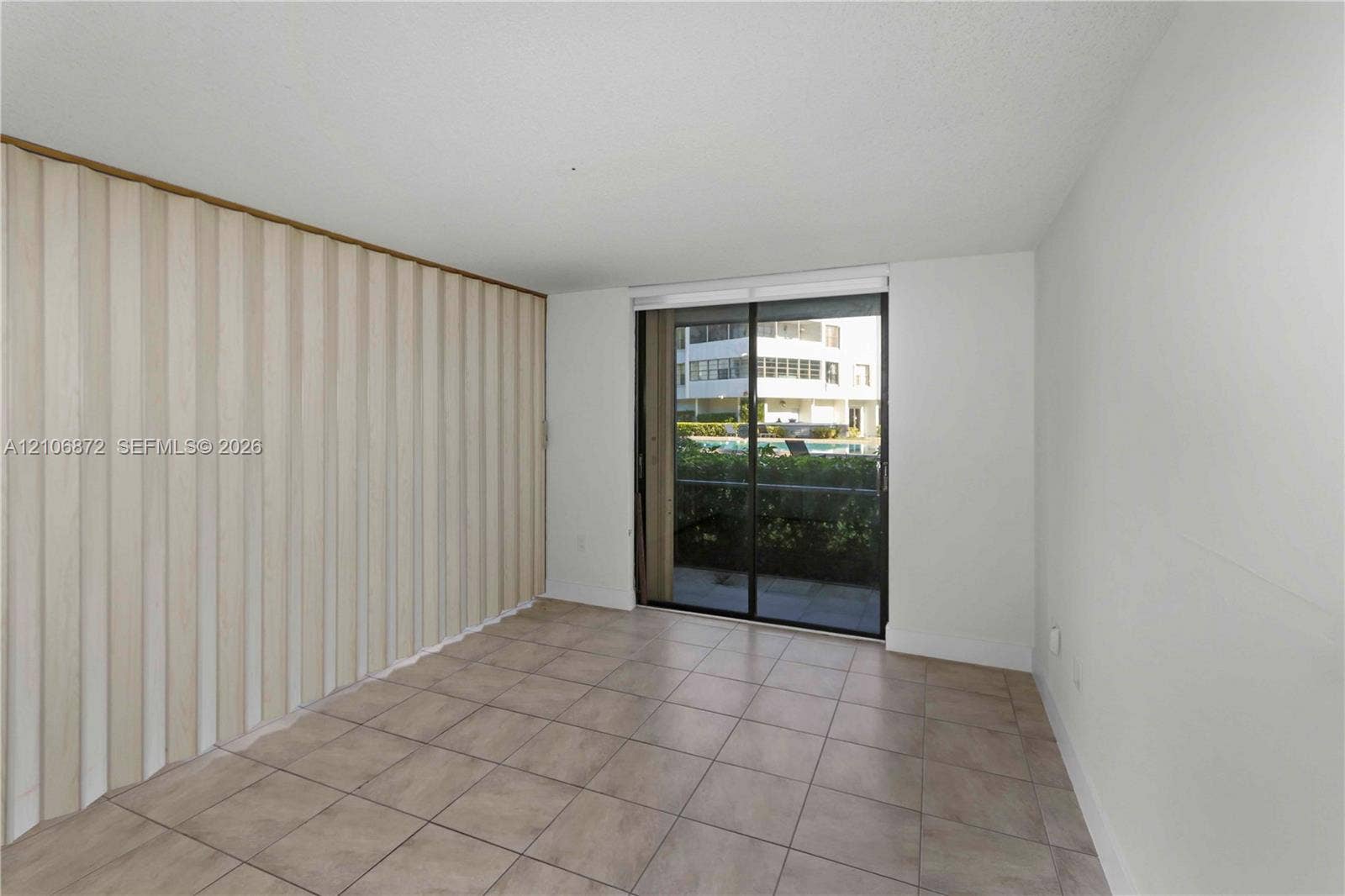 Room with neutral ceramic tile flooring, floor-to-ceiling accordion partition wall, and sliding glass door