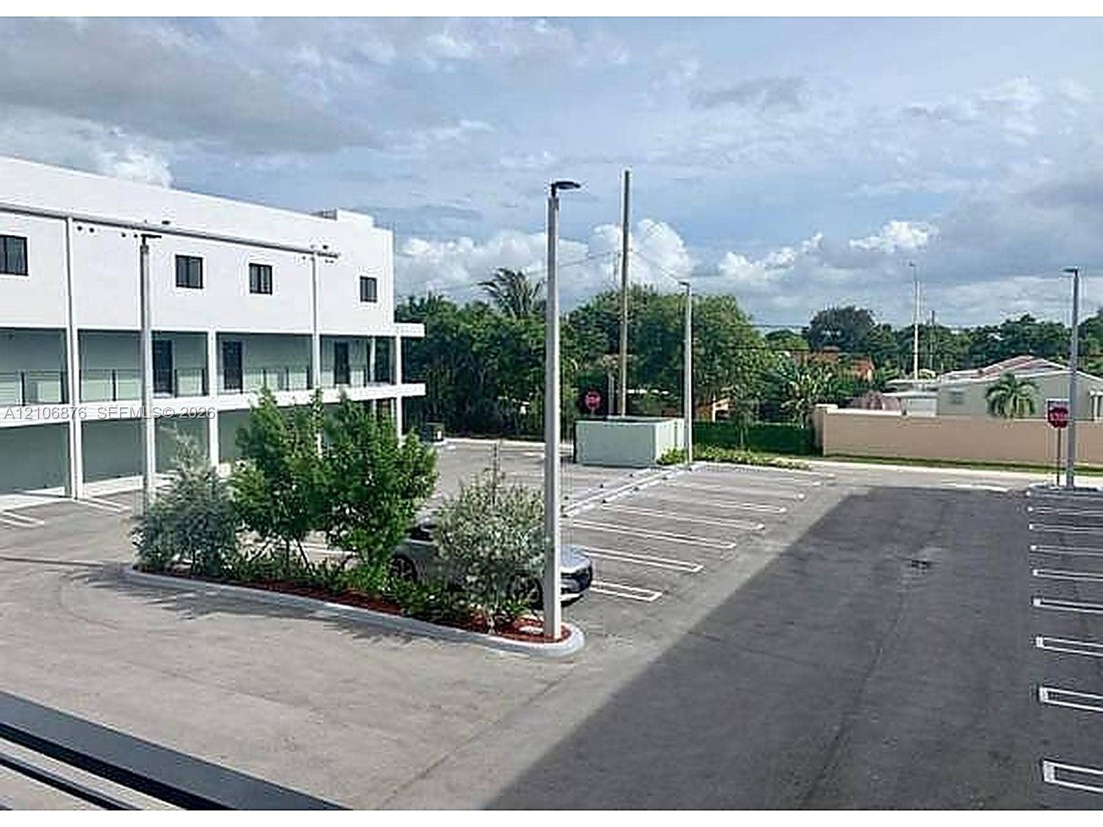 Multi-story building exterior featuring a dedicated paved parking lot, designated parking stalls, asphalt surfaces, integrated post lighting, and mature landscape plantings