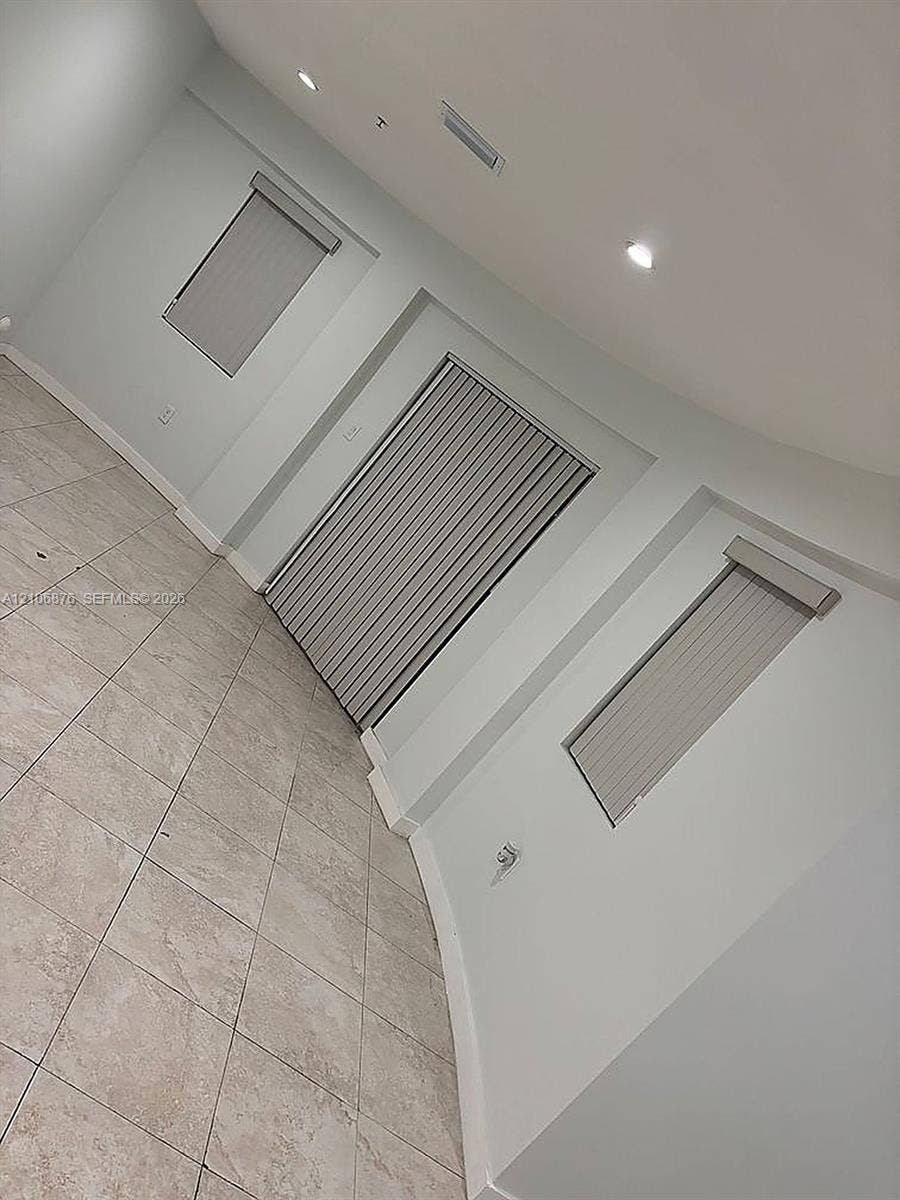 Neutral-toned tile flooring, recessed ceiling lighting, and vertical window blinds