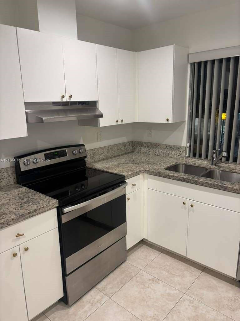 Kitchen featuring white cabinetry, stone-finish countertops, stainless steel range with overhead hood, dual-basin stainless steel sink, and ceramic tile flooring