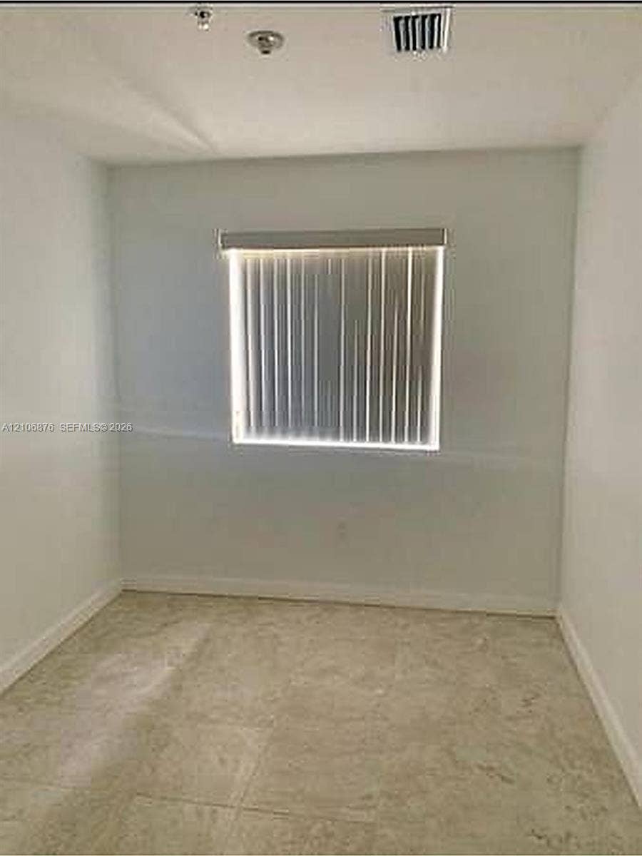 Neutral interior space featuring tile flooring and a window with vertical blinds