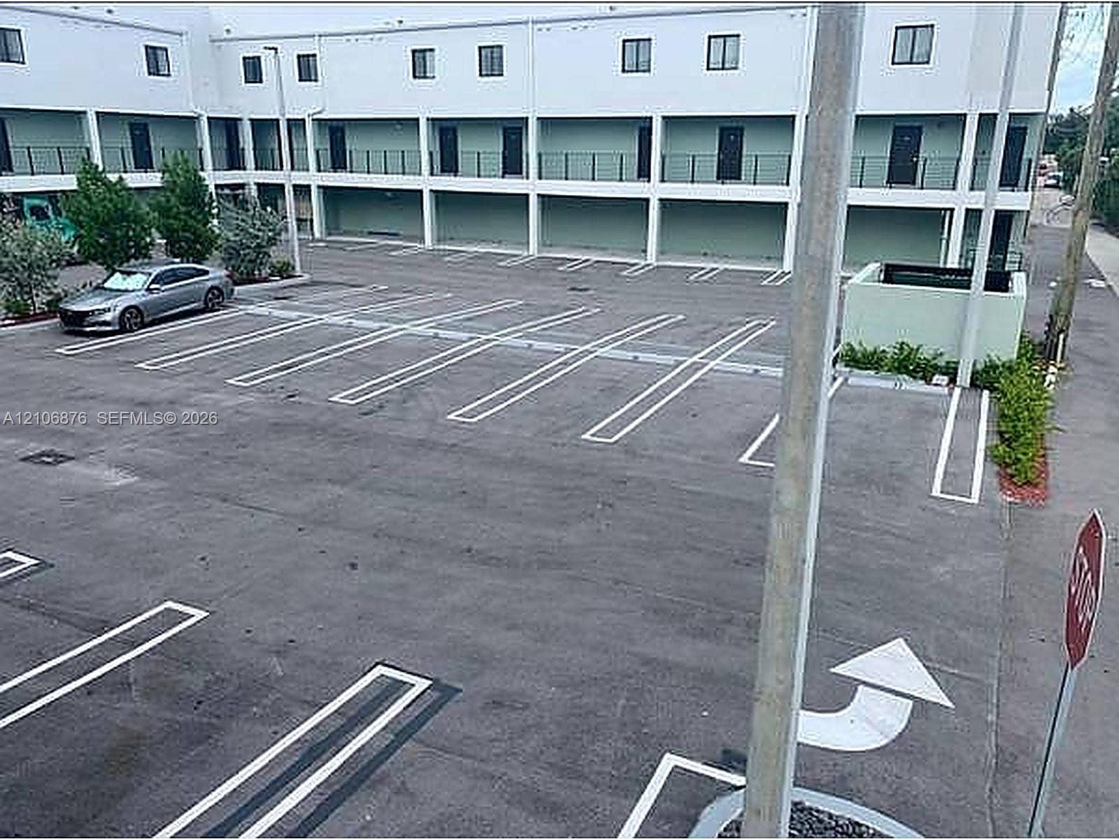 Asphalt parking area with painted stalls, multi-level building exterior with individual entry doors, and metal railings