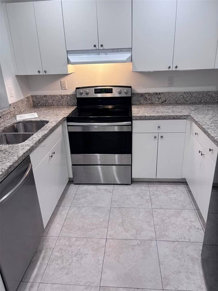 Kitchen featuring white cabinetry, stone-surface countertops, stainless steel appliances, a double-basin undermount sink, and tiled flooring