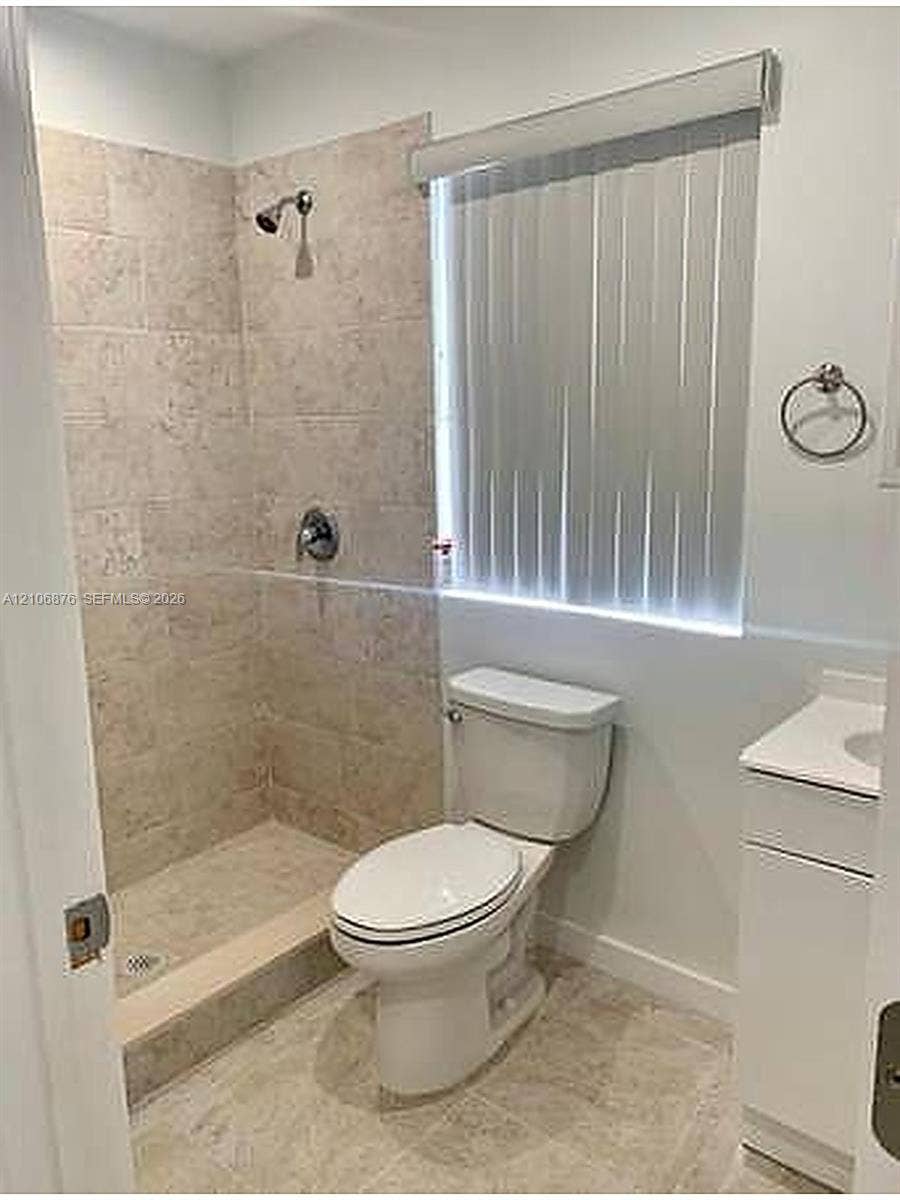 Walk-in shower featuring neutral stone-finish tile surround and flooring, complemented by a white vanity with an integrated countertop and a wall-mounted circular towel ring