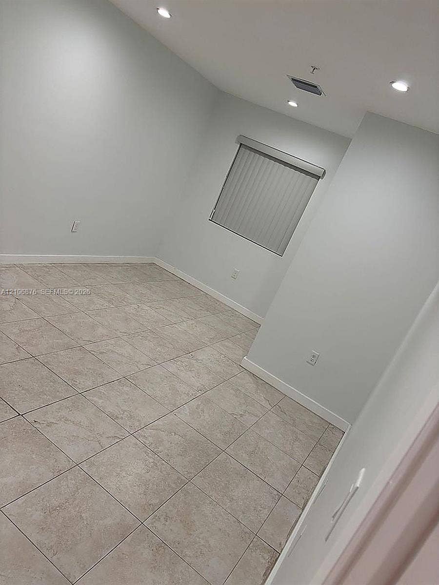Neutral-toned interior space featuring large-format ceramic tile flooring, recessed ceiling lighting, and a single window with vertical blinds