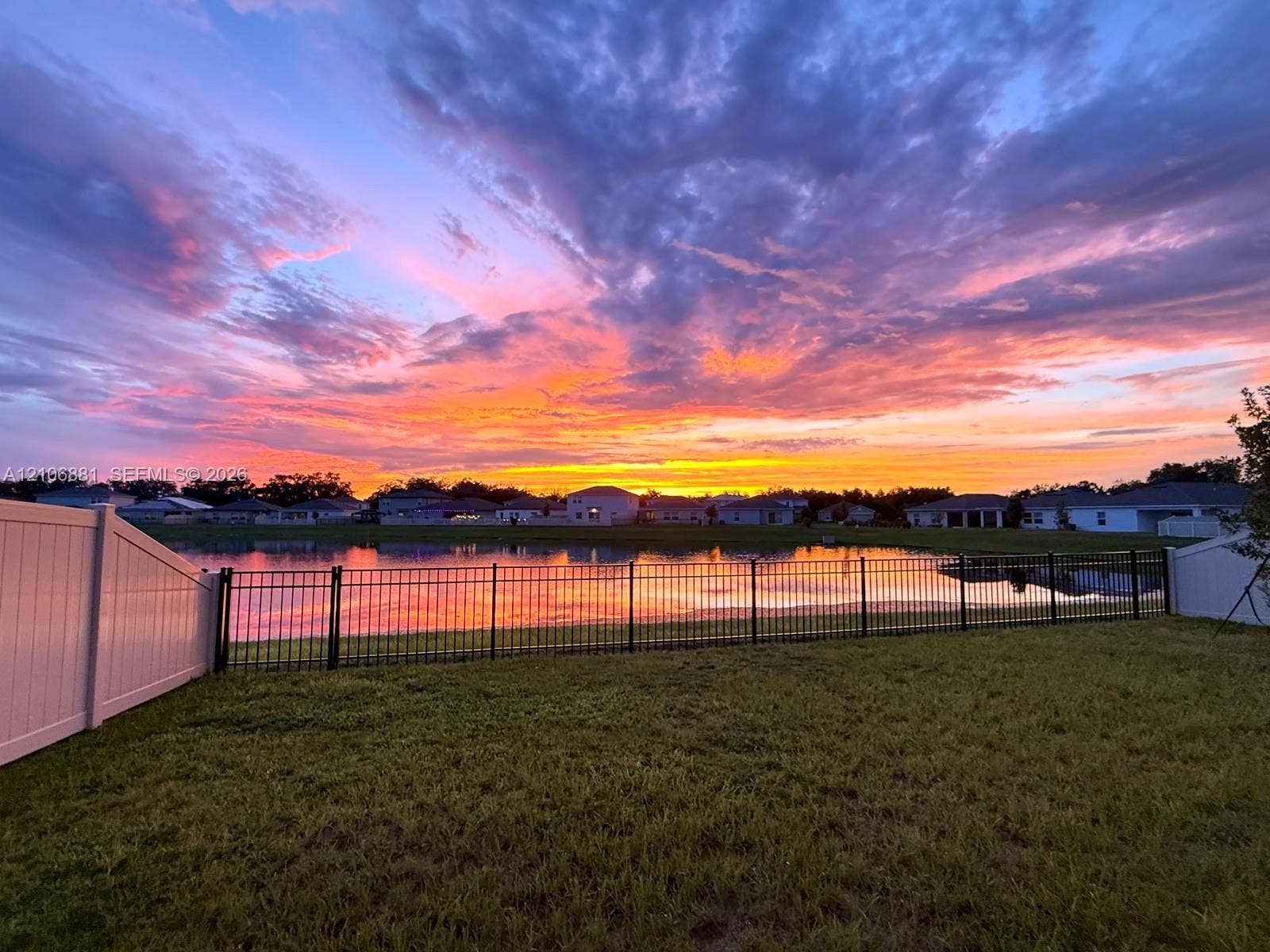 Backyard featuring a grass lawn, metal perimeter fencing, white vinyl privacy fencing, and a waterfront setting