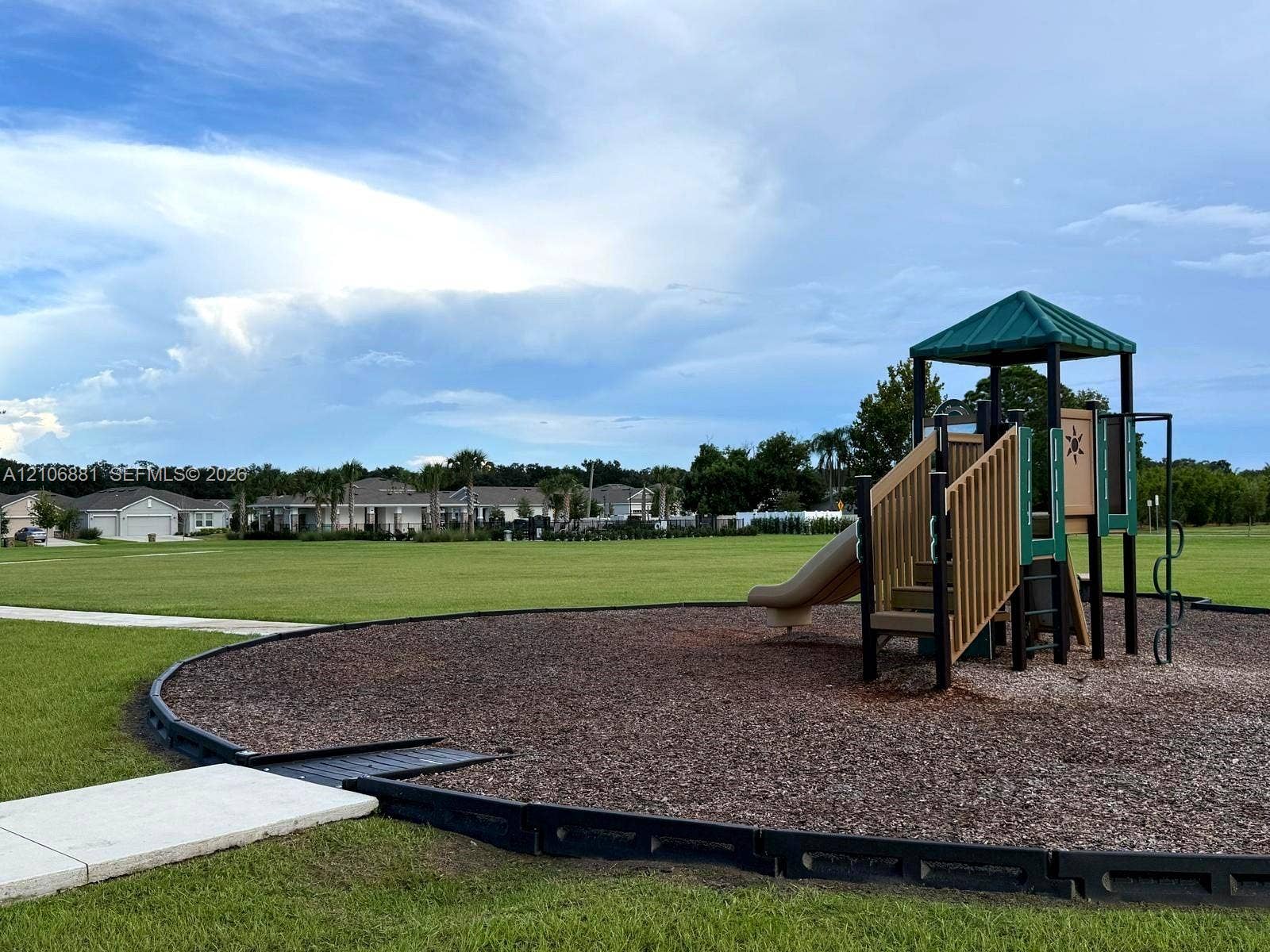 Outdoor recreational area featuring a playground structure with a slide, contained within a mulched border, set on an expansive open lawn